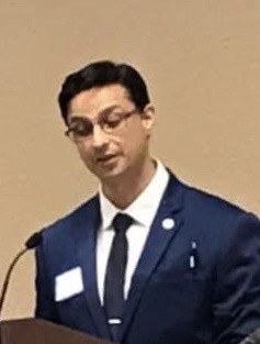 CEO, Shankar Poncelet in suit and tie, speaking in front of podium at San Antonio Free Market Medical Association meeting